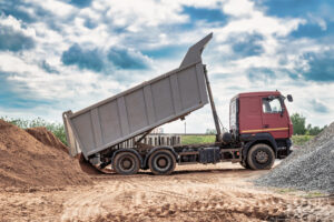Dump truck with a raised body at a construction site. Transportation and unloading of sand or soil. Technique for transportation of bulk materials. Transportation of bulk building materials.